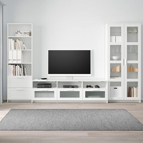 Mueble de TV BRIMNES con estantes y cajones. Centrado en la televisión, los libros, la decoración. Alfombra gris, suelo claro.
