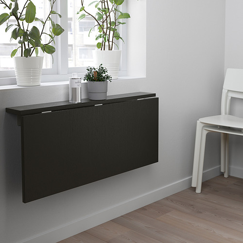 Mesa de pared plegable negra con silla blanca y plantas en maceta.