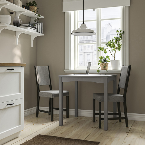 Juego de comedor compacto con mesa gris y sillas a juego cerca de la ventana, estantes blancos, pisos de madera clara.