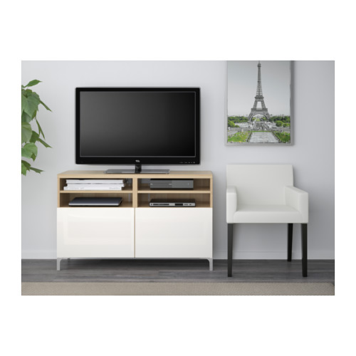 Salón moderno con mueble de TV BESTÅ, pantalla plana, cableado organizado, sillón blanco, póster de la torre Eiffel.