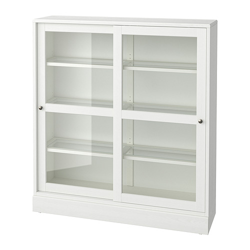 Un mueble blanco con puerta de cristal HAVSTA. Es rectangular con tres estantes en cada sección, puertas correderas de vidrio y un acabado rústico en pino.