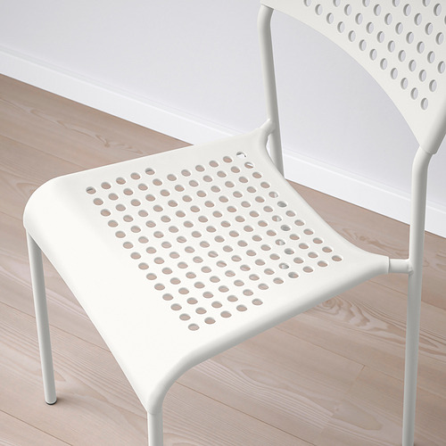 Silla blanca moderna con asiento y respaldo perforados, patas robustas sobre suelo de madera clara.