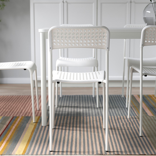 Tres sillas blancas apilables sobre alfombra de rayas de colores. Perfecto para asientos adicionales y fácil almacenamiento.