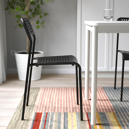 Silla apilable negra ADDE junto a mesa blanca sobre alfombra de rayas, apta para uso en interiores.