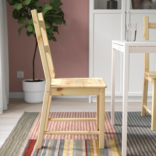 Silla de madera cerca de mesa blanca sobre alfombra de rayas. Habitación luminosa y minimalista con planta.