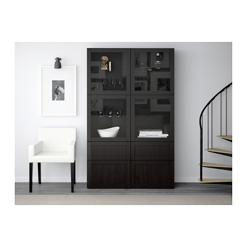 Sala de estar moderna con mueble BESTÅ, artículos de decoración y copas de vino. Silla blanca, escalera, barandillas negras.