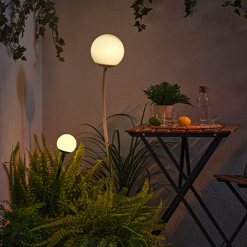Pequeña mesa con plantas en macetas y globos de luz, iluminada por la noche.