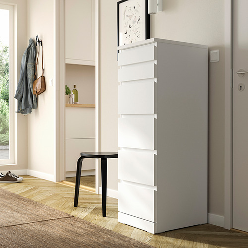 Moderno cofre MALM blanco al lado de la puerta, más pequeño que los ganchos para abrigos, sobre un taburete negro.