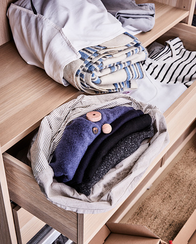 Estante de madera clara KOMPLEMENT, ropa doblada que incluye artículos azules, blancos, a rayas y negros. Almacenamiento de armario ordenado y organizado.