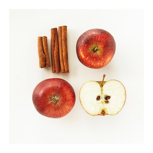 Cuatro manzanas mostradas en diferentes estados: dos enteras, una cortada por la mitad que revela las semillas y la pulpa, tres ramas de canela. Colores simples, naturales, rojos y marrones.