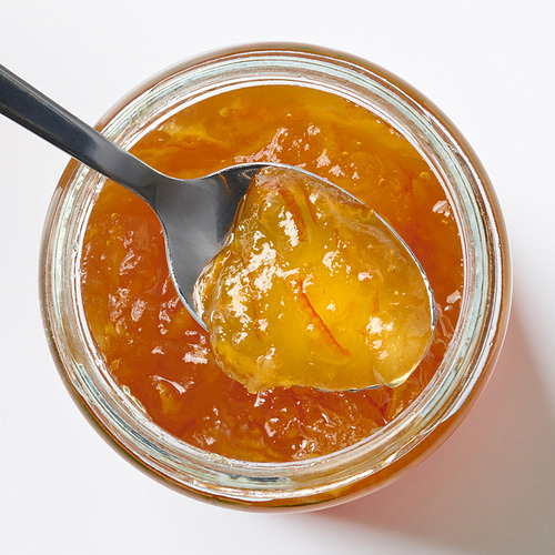 Tarro de mermelada de naranja brillante con cuchara negra, colocada sobre blanco.