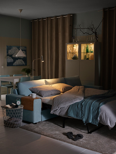 Acogedora sala de estar oscura con sofá cama azul claro, mesa de bandeja de madera y gabinete de curiosidades.