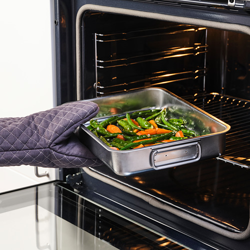 Persona con guantes de cocina colocando una bandeja de metal con verduras de colores en el horno.