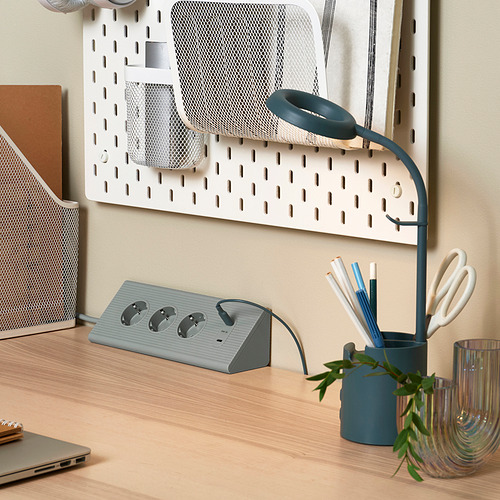 Lámpara azul, cable de extensión gris con puertos usb y organizadores de tablero de clavijas sobre escritorio de madera.