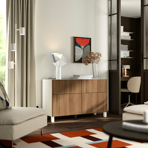 Salón moderno con aparador BESTÅ , cajones de madera, lámpara blanca, alfombra de colores y cortinas beige.