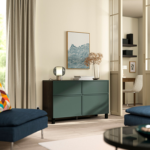 Aparador verde BESTÅ con 4 compartimentos entre sillones azules en sala de estar moderna.