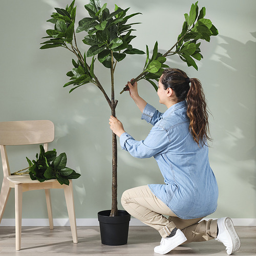 Una mujer monta la planta FEJKA, una vegetación en maceta de interior y exterior realista hecha con plástico reciclado.