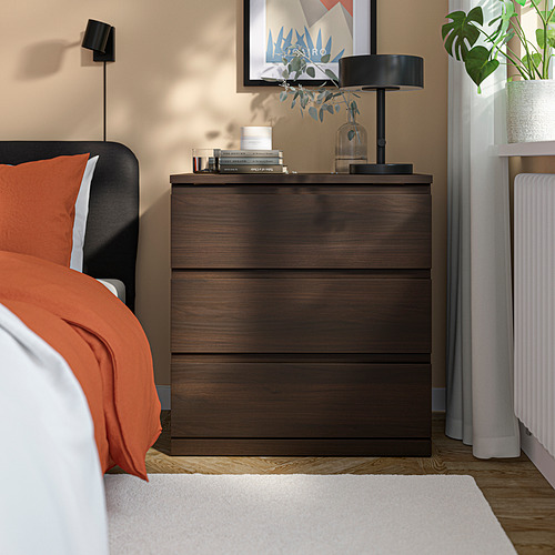 Cofre de noche STORKLINTA de madera oscura; Incluye cajones, lámpara, libros y jarrón. Colocado al lado de la cama, más pequeño que la cama.
