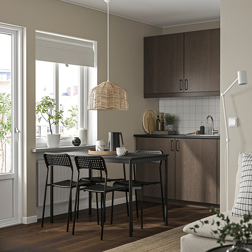 Cocina moderna con sillas de sandberg, mesa redonda, lámpara de mimbre. Cocina americana a la derecha, sofá delante.