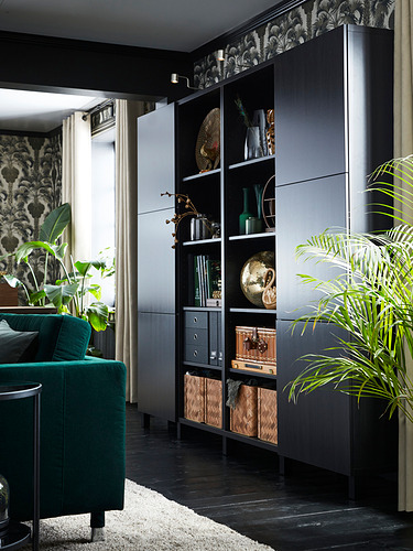 Sala de estar moderna con unidades de almacenamiento negras create & BESTÅ, sofá verde, jarrones decorativos y plantas de pared.
