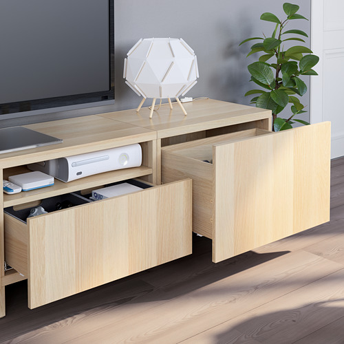 Mueble de TV de madera clara con cajones abiertos, aparatos electrónicos y una lámpara.