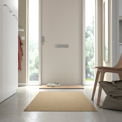 La alfombra LÄTTBETONG beige en el pasillo, cerca de la puerta y la silla, complementa la decoración minimalista.