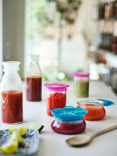 Cubiertas de silicona de varios colores en frascos y tazas, almacenando líquidos rojos y verdes, en una encimera de cocina.