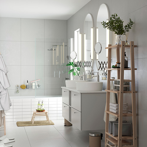 Moderno cuarto de baño blanco con estantería de madera. Tiene múltiples estantes que contienen toallas y plantas. La pared tiene espejos y un elegante lavabo con iluminación.
