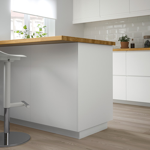 Una moderna isla de cocina blanca con encimera y armarios de madera. Una planta en maceta agrega vegetación.