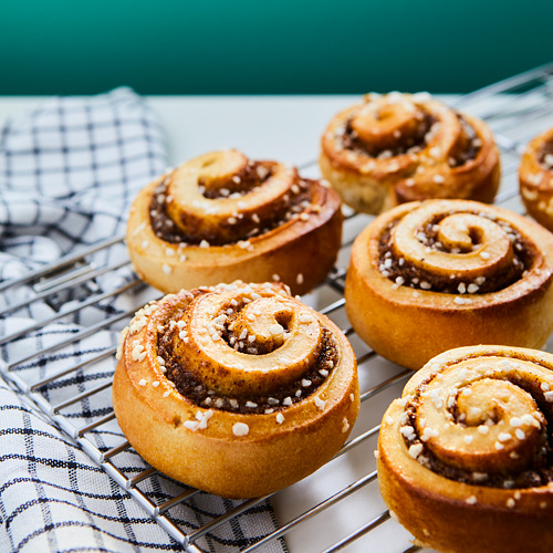 Seis bollos de canela de color marrón dorado con cristales de azúcar descansan sobre una rejilla sobre un paño azul y blanco.