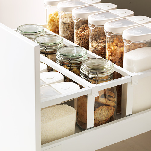Cajón de cocina organizado con varios alimentos en frascos de vidrio transparente y recipientes de plástico, que muestra un almacenamiento ordenado.