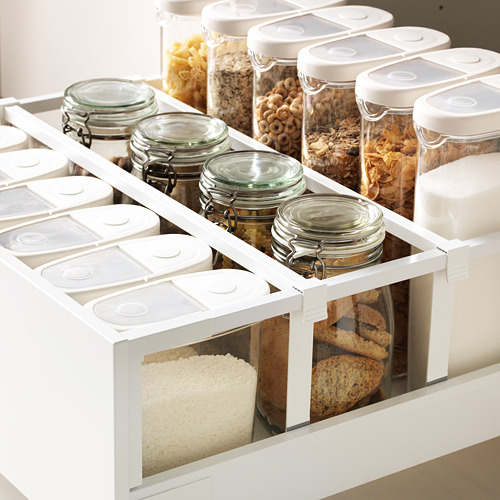 Cajones de almacenamiento de cocina blancos con frascos transparentes que contienen varios alimentos, cuidadosamente organizados. Los cajones están diseñados para extraerse completamente para facilitar el acceso.