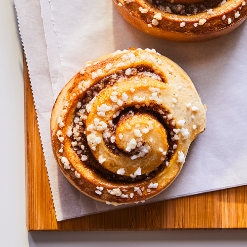 Dos rollos de canela de color marrón dorado cubiertos de cristales de azúcar sobre una tabla de madera.