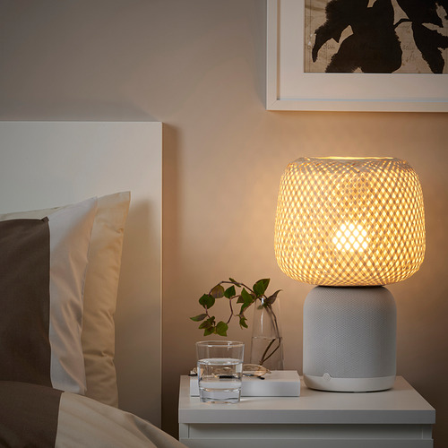 Lámpara SYMFONISK con pantalla tejida en la mesita de noche, agua, planta, cojines, cuadro.