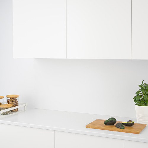 Encimera de cocina con aguacates en una tabla de cortar, frascos y una planta verde. Encimera y salpicadero de cuarzo blanco.