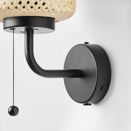 Lámpara de pared de bambú con brazo negro, cordón, diseño natural/moderno sobre pared blanca.