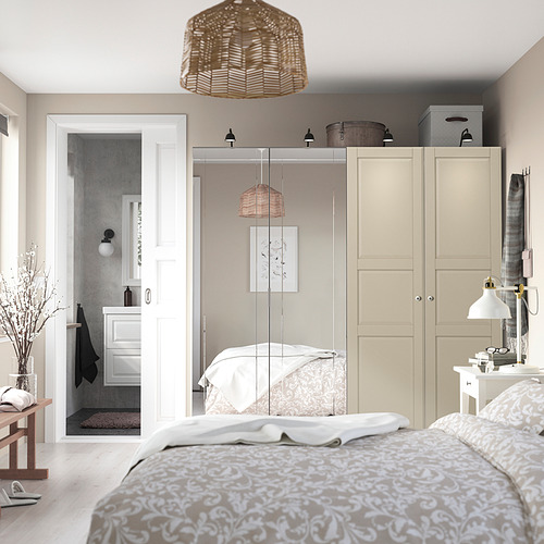Acogedor dormitorio con gran armario PAX, puertas con espejos, luces colgantes, ropa de cama color crema y mesita de noche de madera con lámpara y decoración.