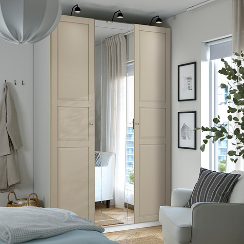 Armario moderno PAX con puertas beige, espejos, bisagras de cierre suave. Cerca, sillón blanco, lámpara y ventana con cortinas transparentes.