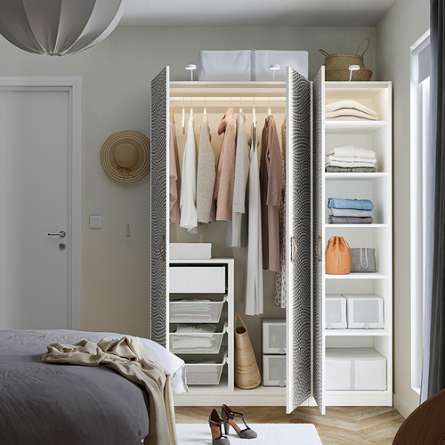 Armario abierto que exhibe prendas, ropa doblada y accesorios entre la cama y la puerta.