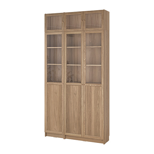Librería BILLY de madera marrón claro con puertas de cristal, diseño moderno y elegante. Altas, rectangulares, con estantes ajustables.