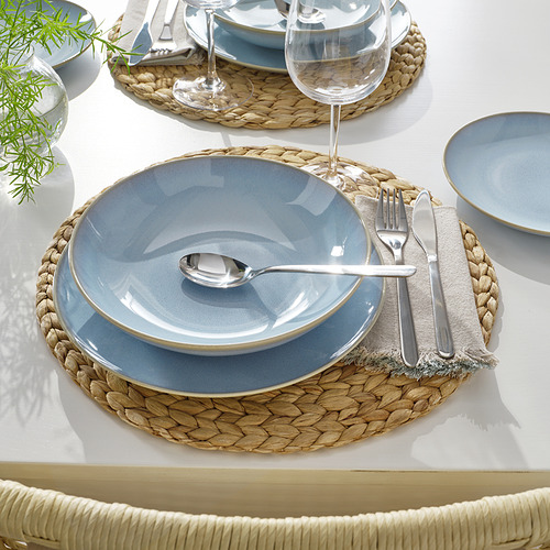 Una mesa con platos y cuencos de color azul claro sobre manteles individuales tejidos, que incluyen cubiertos y copas de vino transparentes.