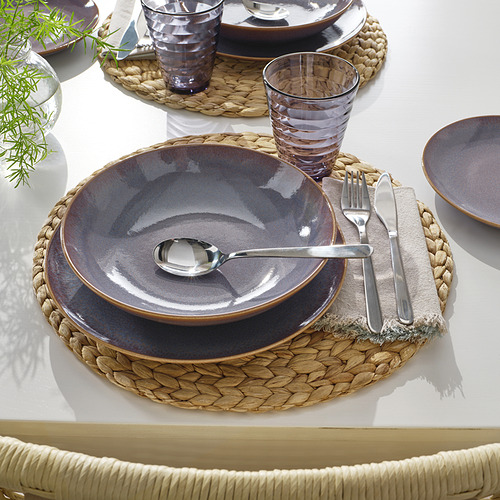 Mesa con vajilla de gres FÄRGKLAR. Incluye plato hondo, tazón más pequeño, utensilios y vidrio en manteles individuales tejidos.