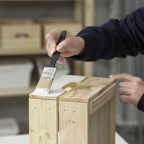 Persona pintando muebles de madera con pintura blanca con un pincel.