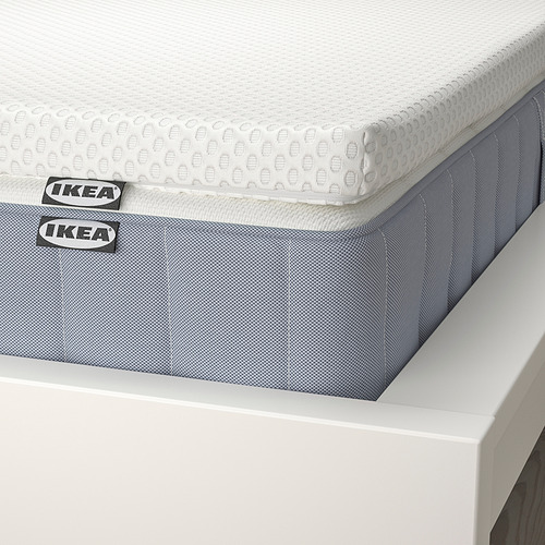 Primer plano del colchón VALEVÅG de IKEA: sobrecolchón blanco, base gris azulada, etiquetas visibles.