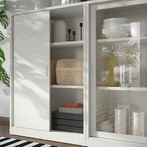 Mueble de almacenaje TONSTAD blanco con puertas correderas y puertas de cristal, con cestas tejidas, jarrones y cajas. Diseño moderno en blanco roto con líneas limpias.