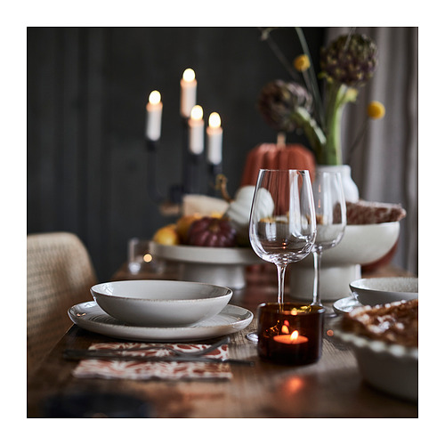 Elegante mesa otoñal con platos blancos, vaso de vino de vidrio transparente y vela ámbar en soporte marrón. El fondo oscuro resalta las decoraciones cálidas.