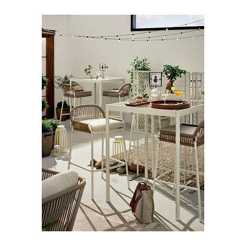 Moderna zona de comedor al aire libre con muebles de metal blanco y mimbre, con pantallas de privacidad LUNGÖN, guirnaldas de luces y plantas en macetas.
