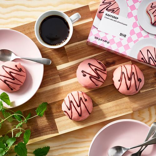 Kit de pausa para el café: pasteles de crema rosa congelados, taza de café, cucharas, en tabla de madera, con empaque de ikea.