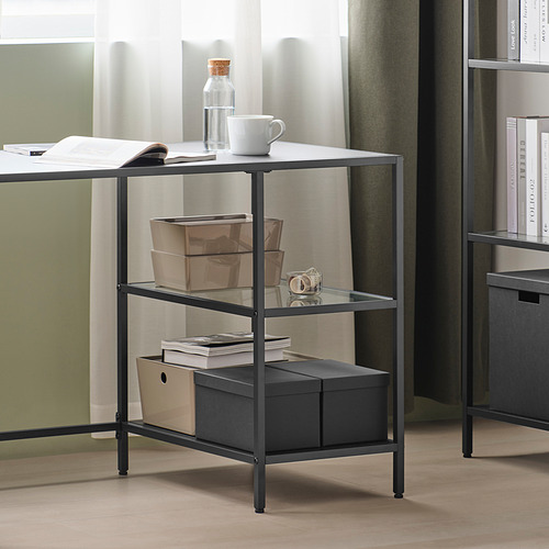 Escritorio moderno de varios niveles con estantes de vidrio templado, cajas de almacenamiento y libros ordenadamente. Incluye una taza blanca y una jarra en la parte superior para mayor comodidad.