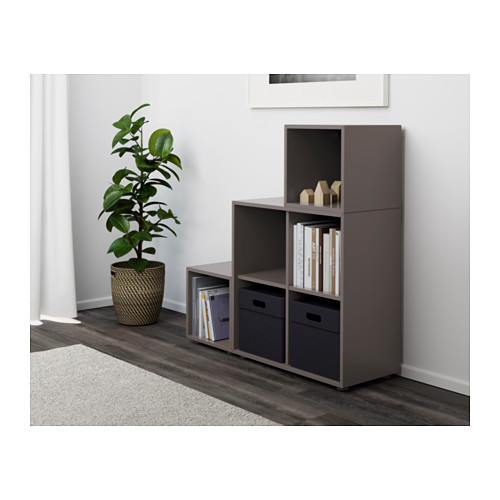 Moderno mueble de almacenaje gris con estantes abiertos, armarios cerrados y dos cajones de tela, con capacidad para libros y planta.